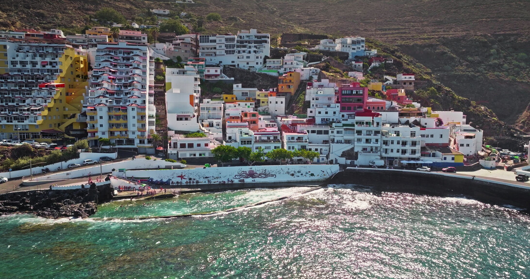 766793 Ablancas - Haznoticia.com Colorful hillside coastal town with whitewashed buildings overlooking a rocky, turquoise sea and a seaside promenade. Note: concise, informative description for screen readers.