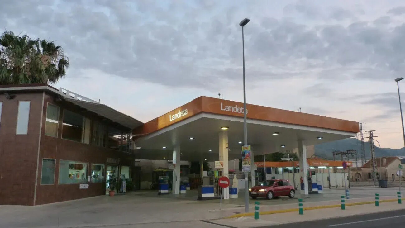 773626 - Gasolinera Landete - Haznoticia.com Gas station with orange canopy labeled 'Landete' and a red car at a pump beside a brick service building on the left.